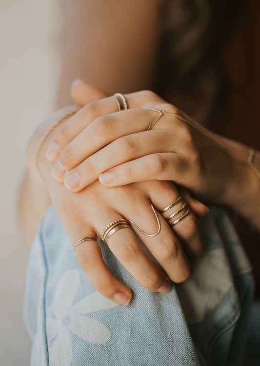 Do you want to know how to stack rings on ringers? Well, Hello Adorn created this ring stack using dainty rings as stacking rings in Confetti Ring, textured rings, thin rings, a U shaped wire ring, a Triple Wrap Ring, and a hand chain bracelet shown in 14k gold fill.